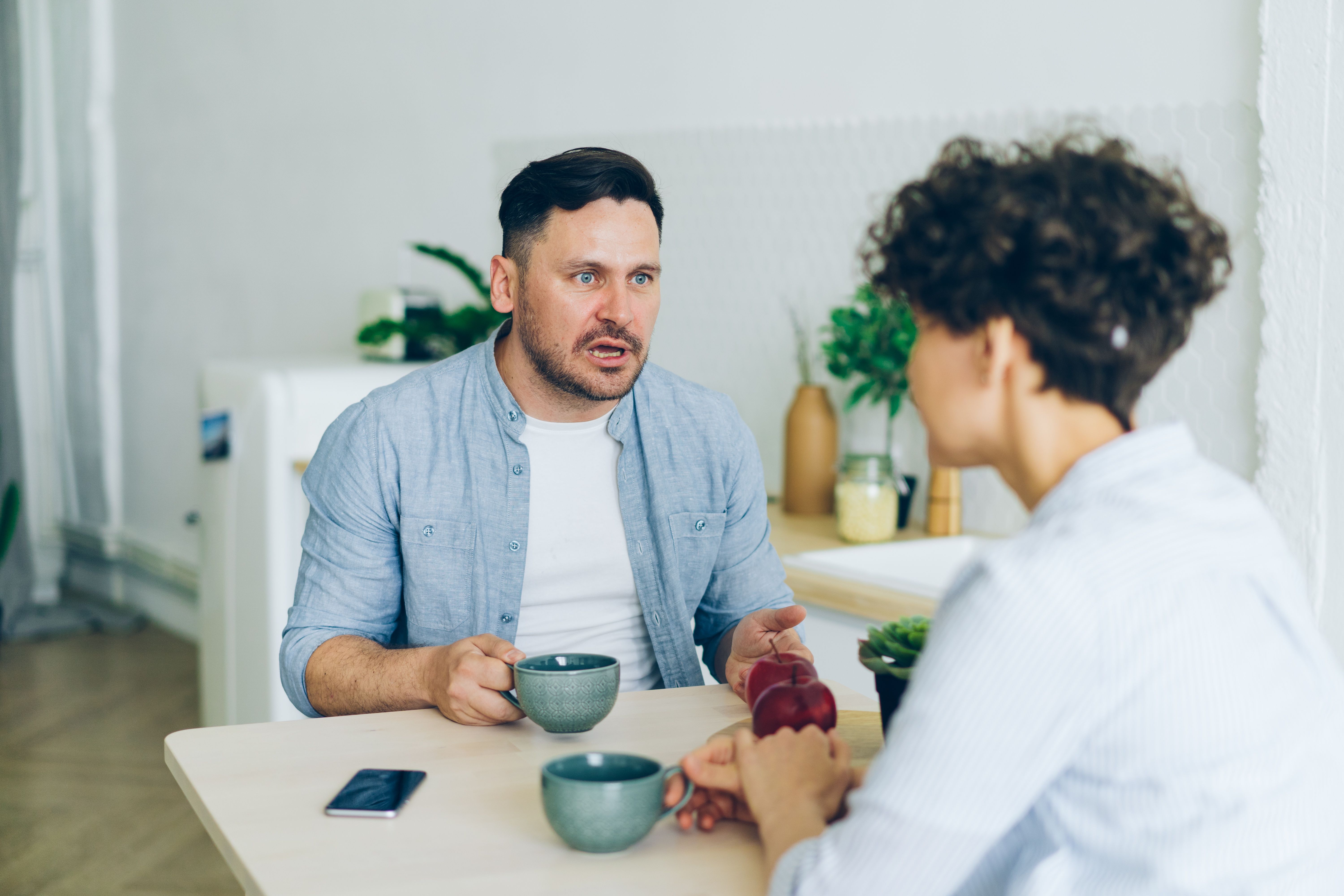 A couple having a serious conversation at a kitchen table, representing open discussion about privacy and boundaries.